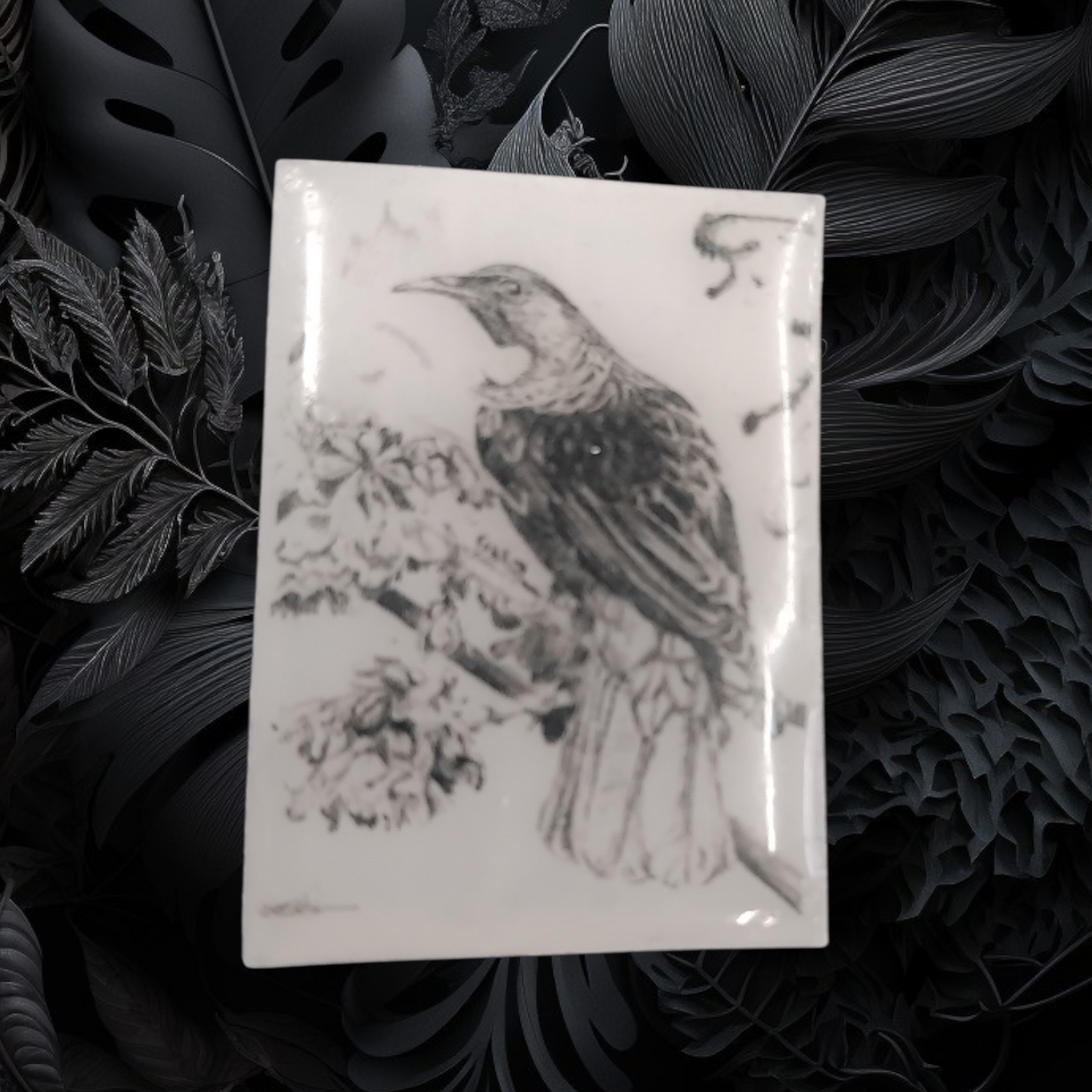 Decorative pin badge with a NZ tui bird design on a dark leafy background