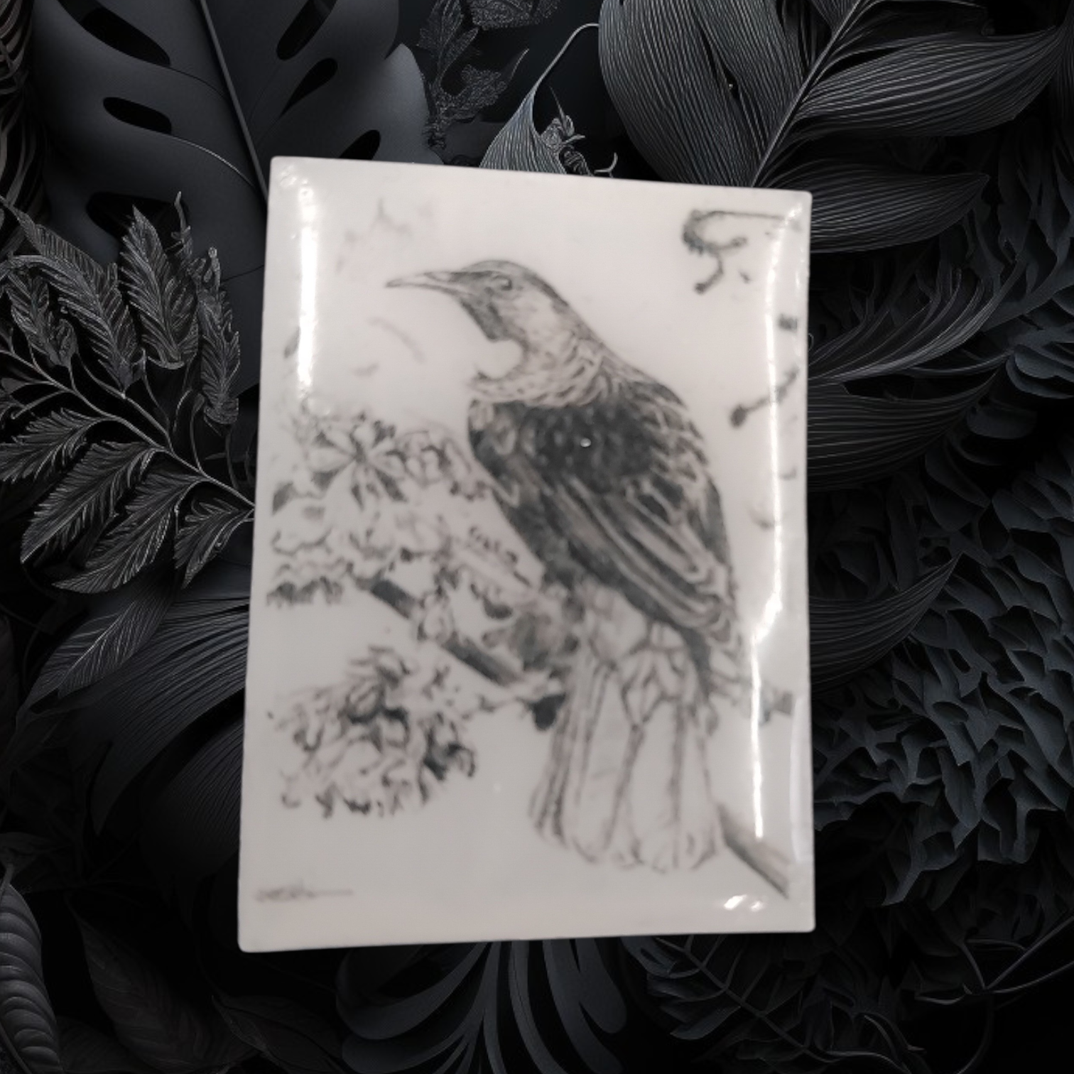 Decorative pin badge with a NZ tui bird design on a dark leafy background
