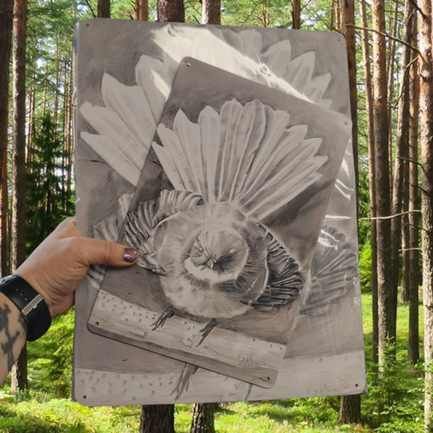 Person holding a drawing of a Piwakawaka nz fantail bird printed on metal in a forest setting