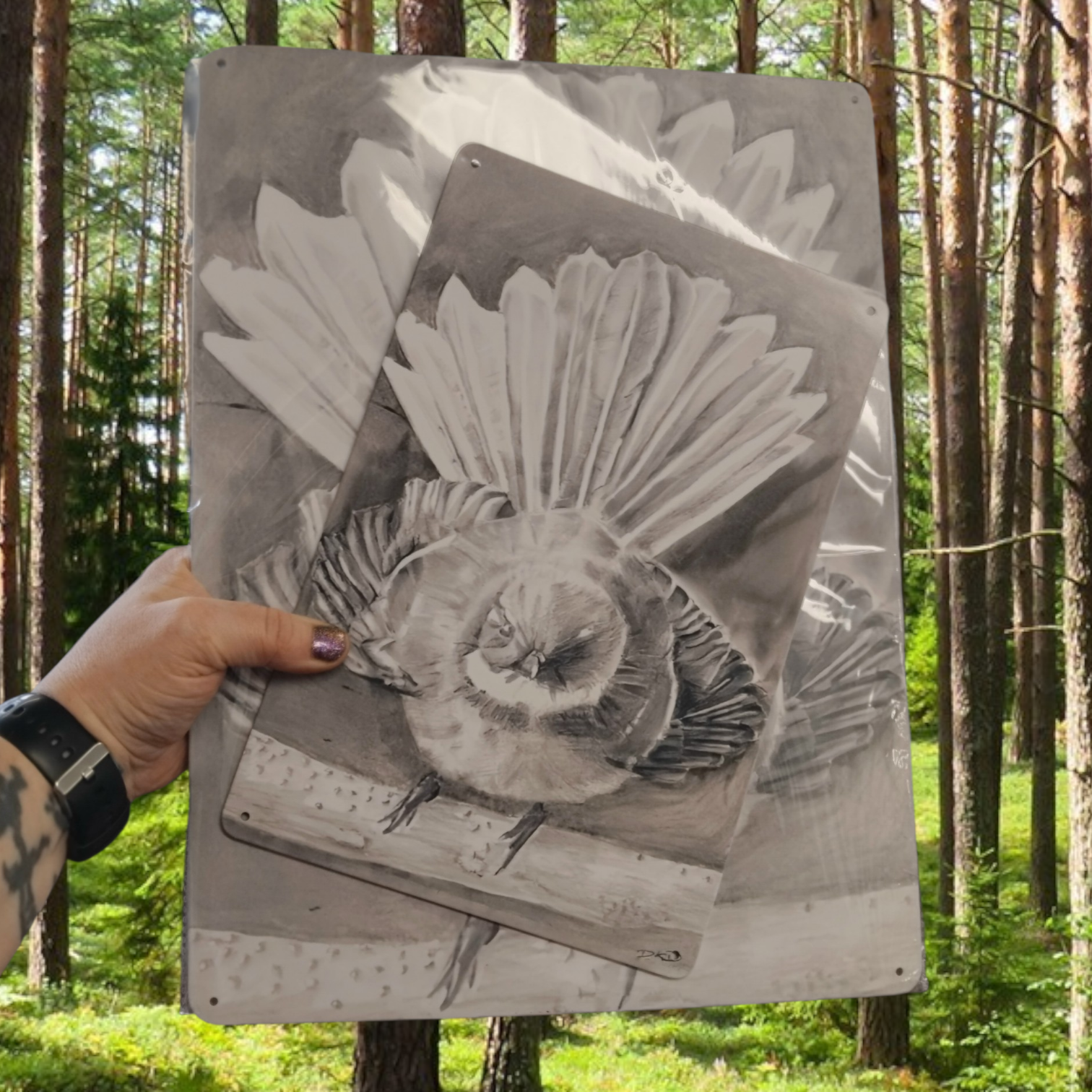 Person holding a drawing of a Piwakawaka nz fantail bird printed on metal in a forest setting